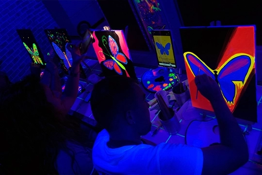 Uno de las mejores experiencia de regalo para tu pareja: pintar con vino en un entorno inmersivo con luces UV y barra libre.