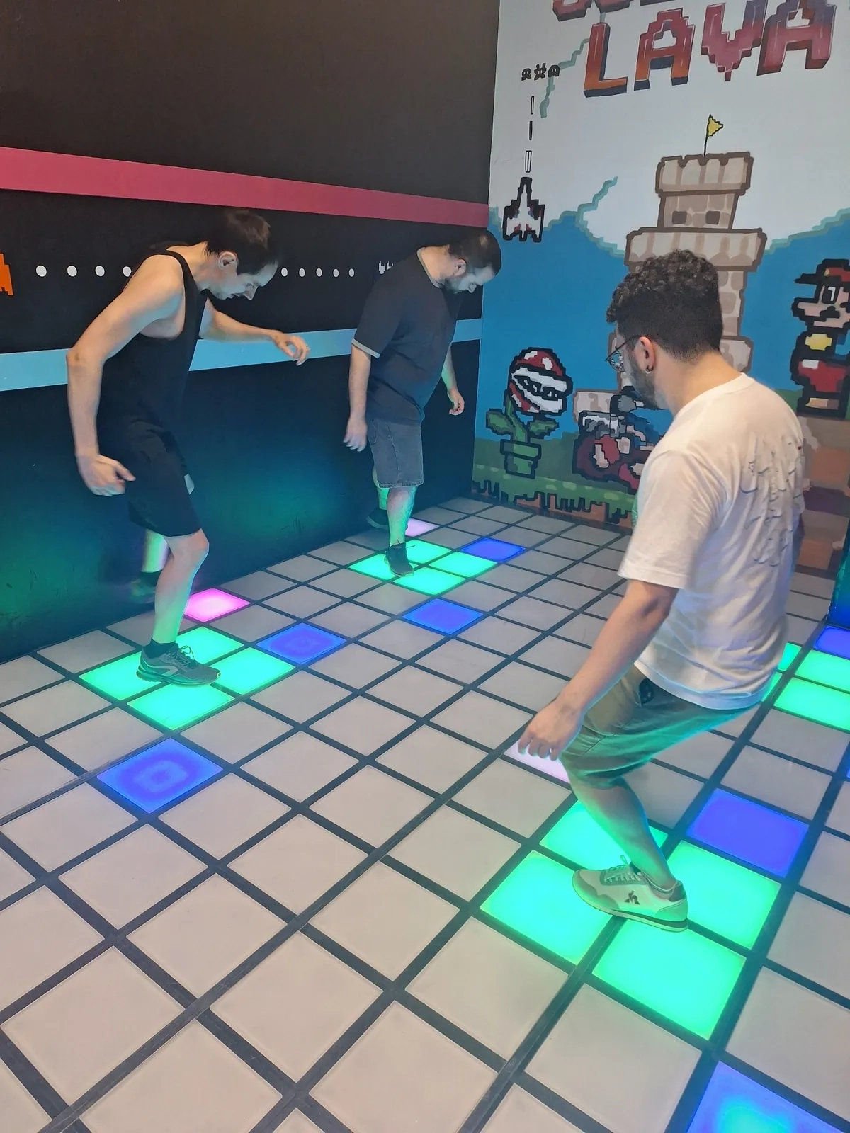 Tres jugadores sobre las baldosas iluminadas de El Suelo es Lava Málaga