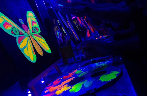 Grupo de amigas pintando lienzos fluorescentes bajo luz negra en Tinto y Tinta Delicias, uno de los planes con amigas en Madrid